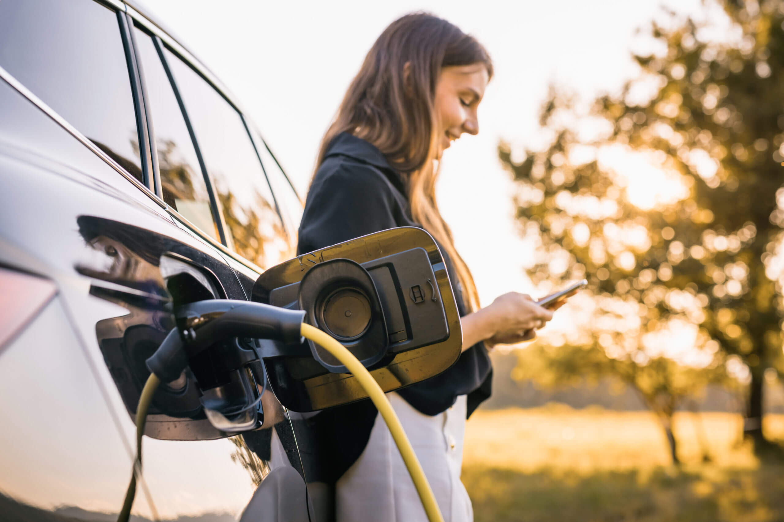 Girl Charging Electric Car And Adjusting An Ev Charging App On Smartphone